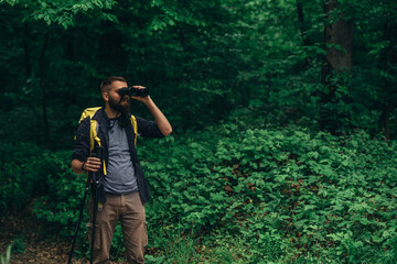 A hiker man walking in the forest using trekking poles and binoculars