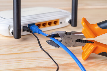 Wire snippers cutting the blue network cable connected to white Wi-Fi wireless router on a wooden...