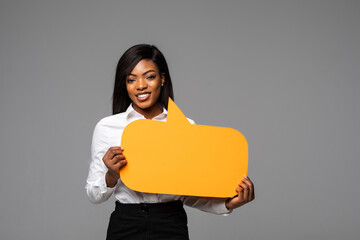 Portrait of happy young african business woman holding empty speech bubble isolated over gray background