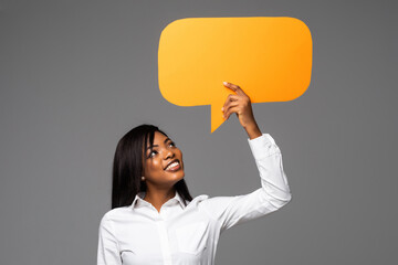 Portrait of happy young african business woman holding empty speech bubble isolated over gray background