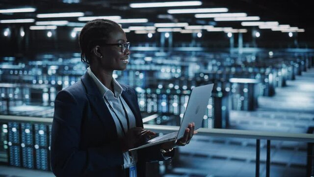 Data Center Female Programmer Using Laptop Computer, Maintenance IT Specialist. In Cloud Computing Server Farm Smiling System Administrator Working on Cyber Security for Iaas, saas, paas. Medium Shot