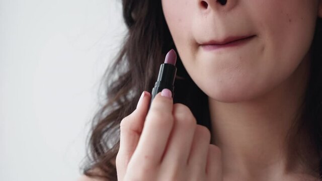 Color cosmetics. Facial makeup. Beauty product. Professional visage. Brunette woman applying brown lipstick on full lips isolated on light copy space background.