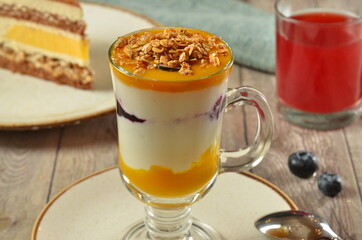 Layered dessert in a glass. Yogurt with granola ( muesli ) and orange jelly. on wooden table rustick background