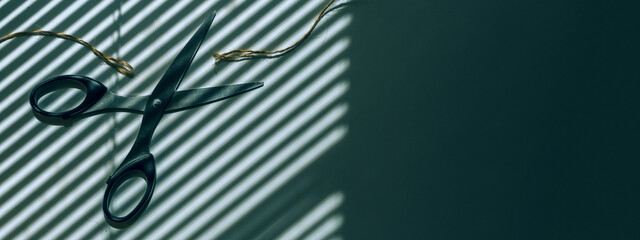 Scissors cut the thread. In the background is a shadow from the blinds. Place for text, hairdresser, office space on the windows of the blinds