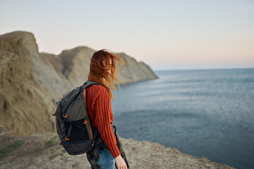 red-haired traveler with a backpack on her back looks at the sea and mountains in the distance