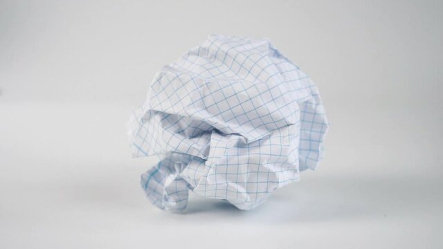 A crumpled ball of empty squared paper sheet falls on the white surface of the table in slow motion. Wrinkled page close up. Creativity and Idea Search Concept