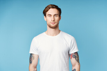 Fototapeta premium man with tattoos on his arms white t-shirt cropped view blue background