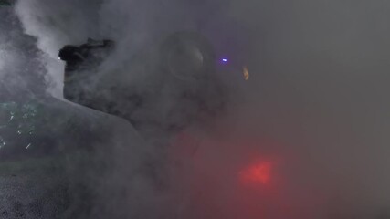 Car Crash Traffic Accident Scene: a burning, heavily smoking car after a road accident, inverted, lies on the street at night