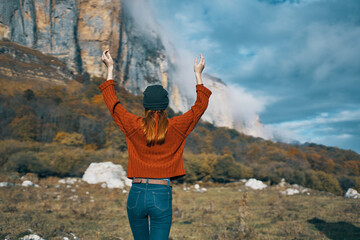 Obraz premium woman in a sweater and jeans with raised up arms travels in the mountains on nature landscape