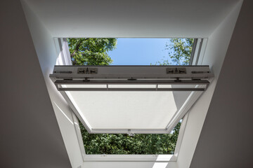 Close up view at slightly opened white Tilt Window Skylights  at attic and defocused of outdoor...