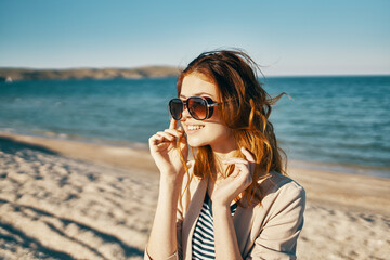 happy red-haired woman in beige jacket and t-shirt on the sand near the sea in the mountains