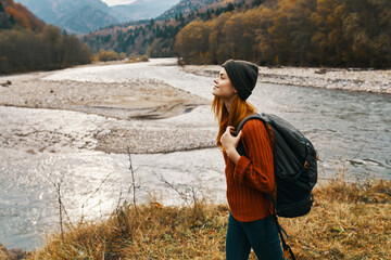 woman traveler with backpack on the river bank in the mountains side view
