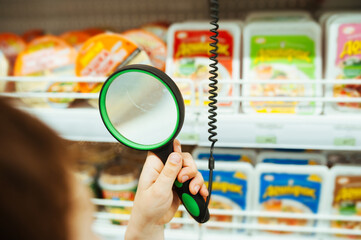 people holds magnifying glass in hand in store and looks at price of product through it. adaptation of stores for people with disabilities. comfortable life with poor eyesight. selective focus