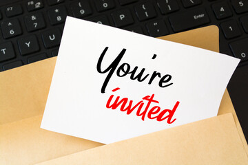 An invitation, An embossed white card with brown envelope on a desk with text You're Invited
