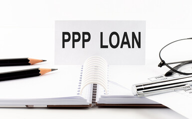 Text PPP LOAN on paper card,pen, pencils, glasses,financial documentation on table - business concept