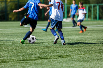 Fototapeta na wymiar Young sport boys in blue sportswear running and kicking a ball on pitch. Soccer youth team plays football in summer. Activities for kids, training 