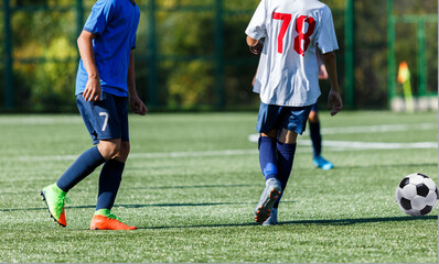 Obraz premium Young sport boys in blue sportswear running and kicking a ball on pitch. Soccer youth team plays football in summer. Activities for kids, training 