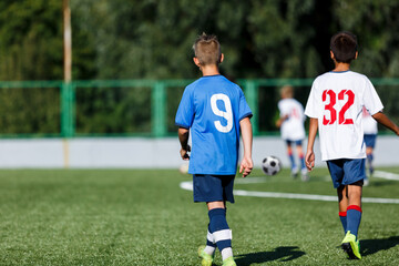 Young sport boys in blue sportswear running and kicking a  ball on pitch. Soccer youth team plays football in summer. Activities for kids, training	