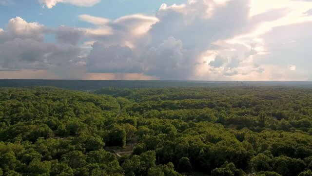 Fly over the green trees of the Ozarks towards giant clouds
