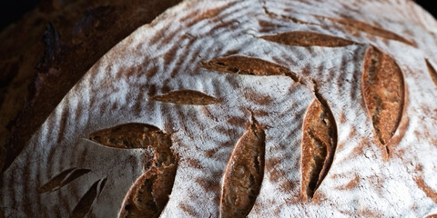 Homemade round dark bread with flour crust and painted spikelet close up on