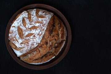 Homemade round dark bread with flour crust and painted spikelet on a clay plate. Top view with copy space