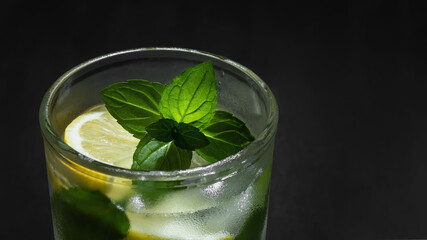 Fresh homemade cocktail with lemon, mint and ice on a dark background close-up