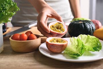 Hand of woman holding sliced passion fruit and preparing vegetables for vegan food cooking on wooden table, Healthy eating