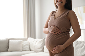 Pregnant young woman touching belly at home, closeup. Space for text