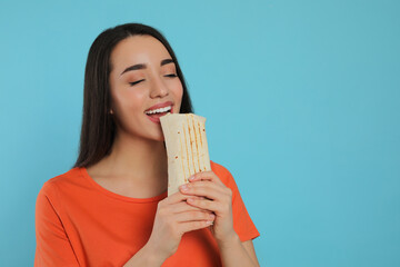 Young woman eating tasty shawarma on turquoise background. Space for text