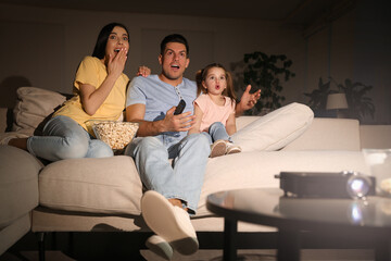 Family watching movie with popcorn on sofa at night