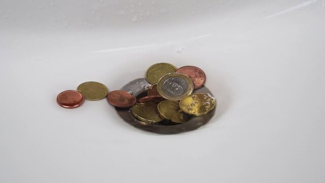Drainage of water through a pile of euro cents in a sink close-up in slow motion. Waste home budget financial concept. Dirty money idea