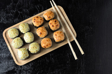 A set of seafood rice rolls wrapped with thin leaves of dried sea grass in a wooden platter on a black wooden background.