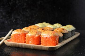 A set of various rolls with chopsticks in a wooden bamboo plate on a black wooden background.