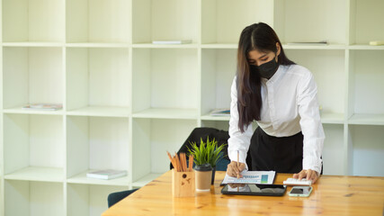 Female office worker with face mask working with paperwork in her office