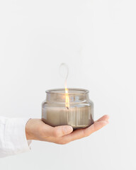 Woman hand holds lit scented candle in glass jar. Wellness and physical, emotional health concept.