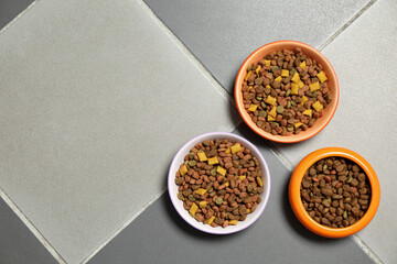 Pet bowls with dry food on floor, flat lay. Space for text