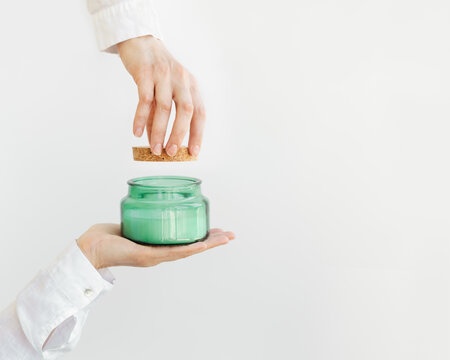 Woman hand holds lid and close scented candle in glass jar with natural ingredients. Wellness and physical, emotional health concept.
