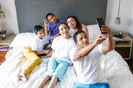 Latin Family And Girl With Cerebral Palsy On Bed At Home Taking A Photo Selfie With Phone In Disability Concept In Latin America