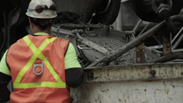 A construction worker overseeing the pouring of concrete from a cement truck.