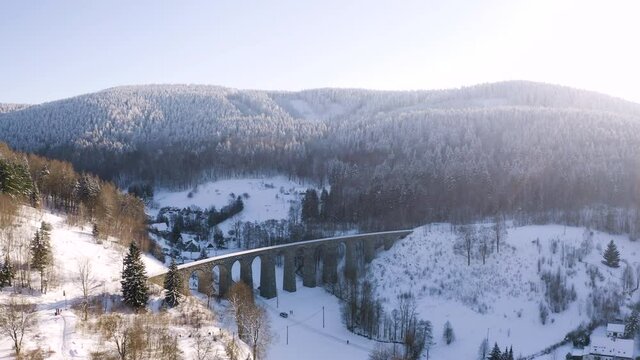 Car driving under a stone train viaduct in snowy winter countryside.