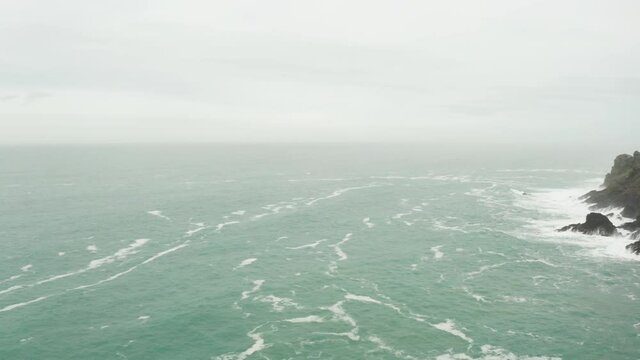 Aerial pan from the roiling Atlantic ocean of the coast of Cornwall to Lands End and the ruins of tin mines perched on the rocky landmass, Cornwall, England.