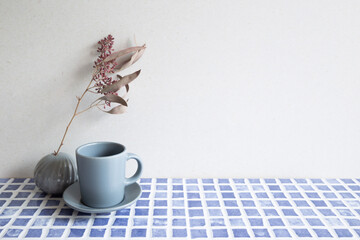 Gray coffee cup and vase of dry flowers on blue ceramic mosaic tile table. white wall background. Home interior - Powered by Adobe