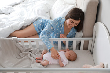Obraz na płótnie Canvas Happy young mother near crib with sleeping newborn baby in bedroom