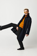 happy man lifted his leg up on a light background and black coat glasses fun shoes