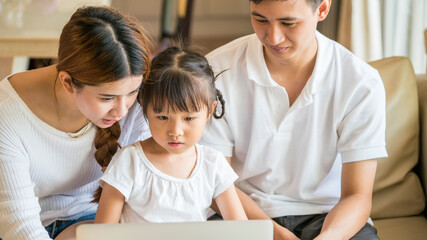 Happy Asian family using laptop computer for online learning a homeschooling in home living room during corona virus pandemic. homeschooling and Asian family concept
