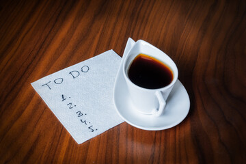 blank to-do list on white napkin and coffee cup on wooden table, personal morning planning concept