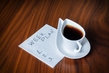 blank week plan on white napkin and coffee cup on wooden table, personal or team planning concept