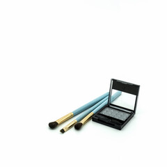 Makeup accessories. Plastic box with gray eyeshadow. Nearby are three blue natural bristle brushes....