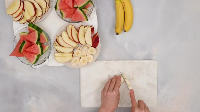 Woman hands slicing bananas, close up video, flat lay.  Fruit salad, healthy delicious desert recipe