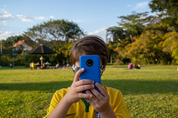 Garoto segurando seu celular e fazendo uma selfie dentro do parque natural 